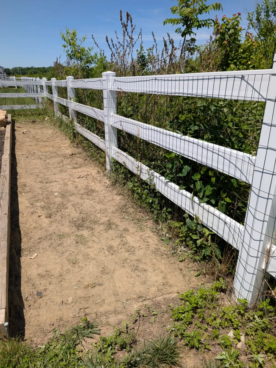Cleared soil along a white fence beside a playhouse area after weeds were removed.